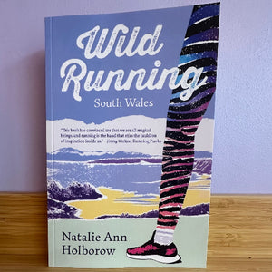 Book titled 'Wild Running South Wales' by Natalie Ann Holborow on a wooden surface with a purple wall background.