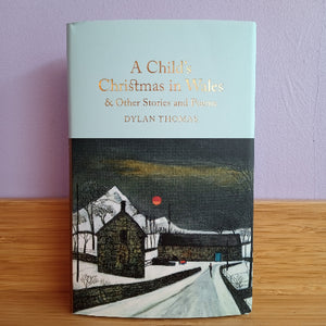 Book titled 'A Child's Christmas in Wales' by Dylan Thomas on a wooden surface with a purple wall background.