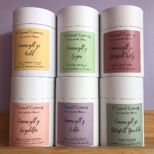 A collection of cylindrical white candles with various labels, displayed on a wooden surface against a purple background.