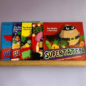 A collection of Supertaten children's books in Welsh, featuring various colorful book covers on a wooden shelf.