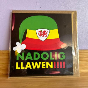 A packaged Christmas card with a green, yellow, and red hat design, featuring text in Welsh and English, and a white flower illustration.