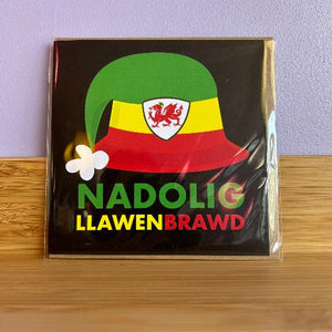 A packaged Christmas card with a green, red, and yellow hat design and the text 'NADOLIG LAWEN BRAWD' on the front.
