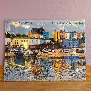 Calendar Cymru 2026 for Wales with a scenic harbor image on a wooden surface.