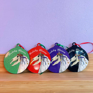 Four circular ornaments with Mari Lwyd designs and colorful backgrounds on a wooden surface.