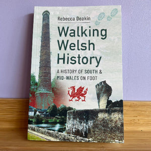 Book titled 'Walking Welsh History' by Rebecca Deakin on a wooden surface with a purple wall background.