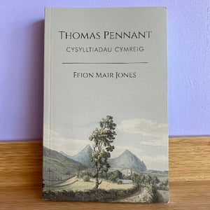 Book titled 'Thomas Pennant' with a landscape illustration on a wooden surface and purple background