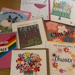 Collection of greeting cards with floral designs and 'Chwaer' text on a wooden surface.
