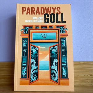 Book titled 'Paradwys Goll' with a decorative cover featuring an open door design on a wooden surface.