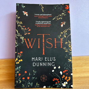 Book titled 'Witch' by Mari Ellis Dunning with floral design on a wooden surface and light purple wall background.