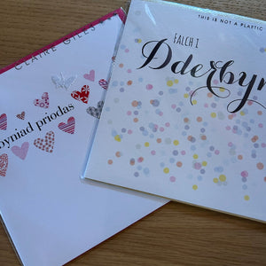 Two greeting cards on a wooden surface, one with heart designs and the other with confetti pattern.