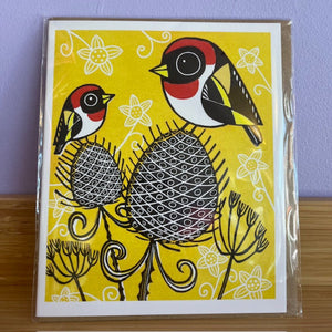 Card with stylized birds and flowers on a yellow background, placed on a wooden surface.