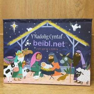 A colorful pop-up book titled 'Y Nadolig Cyntaf' featuring a nativity scene with cartoon characters and a Christmas tree on the cover.