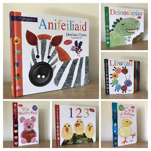 A collection of children's bilingual books in English and Welsh with various colorful animal and shape illustrations.