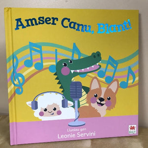 Children's book cover titled 'Amser Canu, Blant!' featuring illustrations of a sheep, a dragon, and a dog with musical notes in the background.
