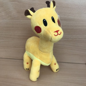 A plush toy representing a yellow giraffe with red cheeks and black eyes, standing upright on a wooden surface.