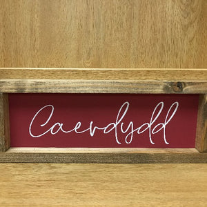 A wooden sign with a red background and white text that reads 'Caerdydd'.