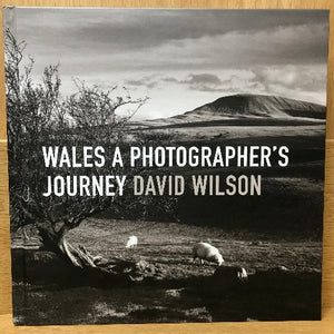 Cover of the book 'Wales - A Photographer's Journey' by David Wilson, featuring black and white photograph of a landscape with sheep and trees in the foreground and hills in the background.