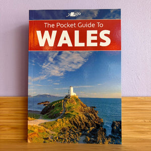 Pocket guide to Wales with a lighthouse on the cover, placed on a wooden surface against a light purple wall.