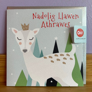 Card with a deer illustration and Welsh Christmas greeting on a wooden surface.
