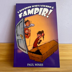Book titled 'Y Diwrnod Wnes i Gwrodd a Fampir!' by Paul Wines on a wooden surface with a white wall background.