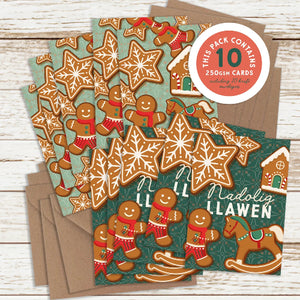 A set of Christmas-themed greeting cards and envelopes displayed on a white wood background. The cards feature festive gingerbread illustrations, including stars, cookies, and a rocking horse, with one card personalized with the name 'Nadlig Llawen' in white text.