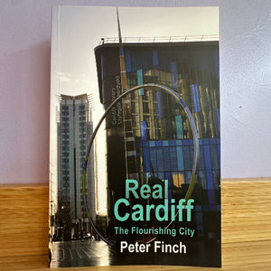 Book titled 'Real Cardiff: The Flourishing City' by Peter Finch on a wooden surface with a light purple wall background.