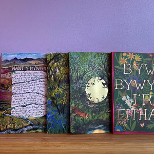 Four books with colorful covers on a wooden surface against a purple wall.