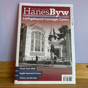 Book titled 'Hanes Byw' with a building image on the cover, placed on a wooden surface.