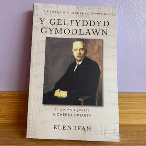 Book titled 'Y Gelfyddyd Gymodlawn' with a portrait on the cover against a light purple wall.