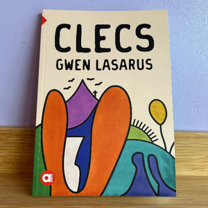 Book titled 'CLECS' by Gwen Lasarus with colorful abstract designs on a wooden surface and light blue wall background.