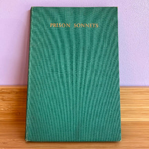 Green book titled 'Prison Sonnets' on a wooden surface with a purple wall background