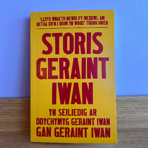Book titled 'STORIS GERaint Iwan' with yellow cover and red text on a wooden surface.