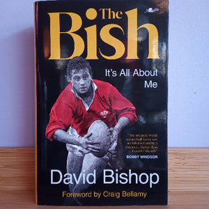 Book titled 'The Bish: It's All About Me' by David Bishop on a wooden surface with a light blue background.