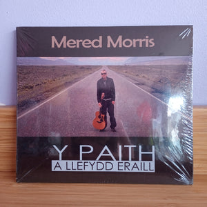 Album cover with a person holding a guitar on a road, featuring the text 'Mered Morris Y Paith A Llefydd Eraill'.