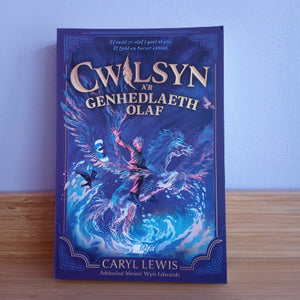 The book 'Cwilsyn ar Genhedlaeth Olaf' by Caryl Lewis, featuring a dark blue cover with an illustration of a warrior riding a blue dragon, displayed on a wooden surface against a light blue wall.
