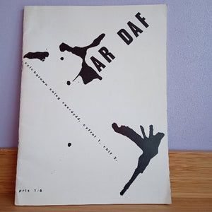 A vintage printed sheet or booklet cover photographed from above, featuring black abstract ink-like splatters and the large text 'AR DAF' on an off-white background, resting on a wooden surface against a light purple wall.