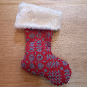 A red Christmas stocking with a gray snowflake pattern and a fluffy cream faux-fur cuff, resting on a light wood surface.