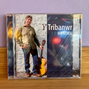 CD cover with a person holding a guitar against a stone wall, featuring the text 'Tribanwr YR HWNTWS'.