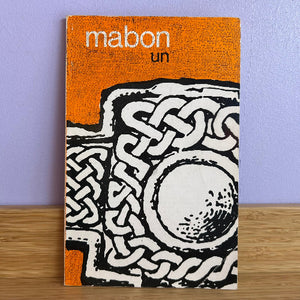 Book titled 'mabon un' with Celtic knot design on an orange and black cover against a purple wall.