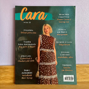 Cara magazine cover from July 2026, featuring a woman in a brown and white polka dot dress, displayed on a wooden surface against a light purple wall.
