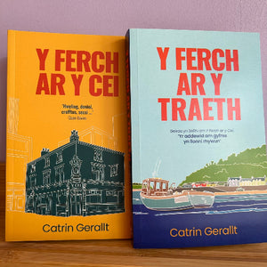 Two paperback books by Catrin Gerallt titled 'Y Ferch Ar Y Cei' and 'Y Ferch Ar Y Traeth' standing side by side on a wooden surface against a lavender wall. The left book has a bright yellow cover with red title text and a dark teal building illustration.