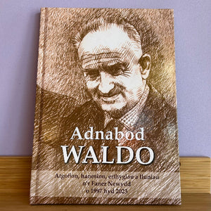 A hardcover book titled 'Adnabod WALDO' with a sepia-toned sketch portrait on the cover, standing upright on a wooden surface against a light purple wall.