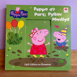 A Welsh children's Peppa Pig picture book by Rily, featuring a green cover with illustrations of Peppa and George, balloons, and muddy puddles.
