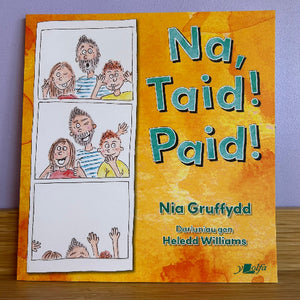 A children's book titled 'Na, Taid! Paid!' by Nia Gruffydd, with a bright orange cover featuring a comic strip of three panels showing a family and the title in large blue letters. The book is photographed standing upright on a wooden surface against a light purple background.