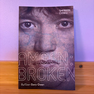 Book cover of 'AMGEN: BROKEN' by Gan Gary Owen on a wooden surface with a purple background
