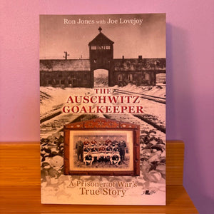 Book titled 'The Auschwitz Goalkeeper' on a wooden surface with a pink background