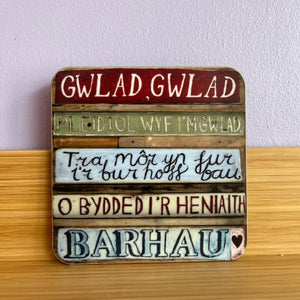 Wooden sign with Welsh text on a wooden surface and light purple wall background
