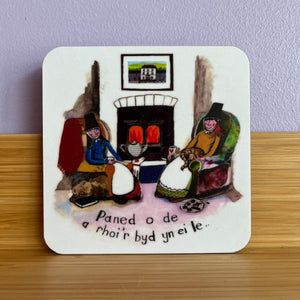 Coaster with a design of people around a fireplace on a wooden surface.