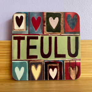 Colorful wooden block design with hearts and the word 'TEULU' on a wooden surface.