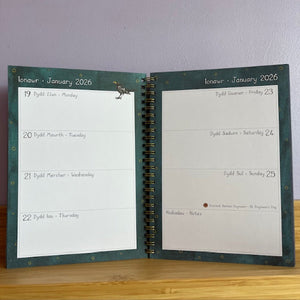 Open planner showing a page from January 2026 on a wooden surface with a white wall background.